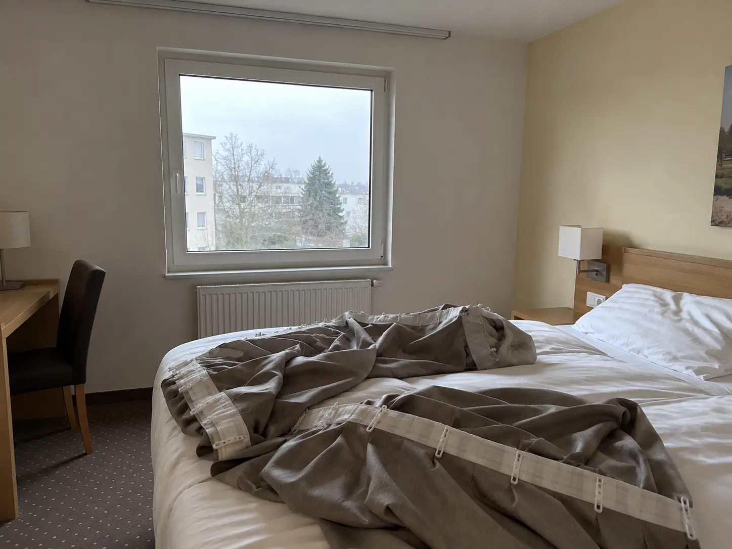 Abgenommene graue Vorhänge mit Gardinenband und Haken liegen zur Reinigung auf dem Hotelbett, im Hintergrund das Fenster